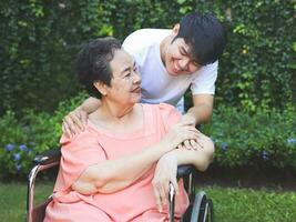 Asian senior woman sitting on wheelchair with her son in the garden. photo