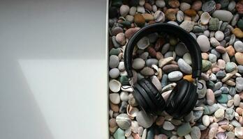 Concept Photo Of Flat Box Filled With Pebbles And Black Headphones On It On A White Surface