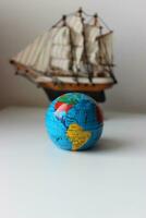 Vertical Image Of Miniature Globe In Front Of Mast Ship Model Isolated On White Backdrop photo