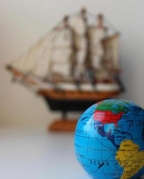 Small Globe With Mapped Travel Routes And Defocused Masted Ship Toy On Background photo