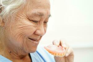 Asian senior woman patient holding teeth denture in her hand for chew food. photo