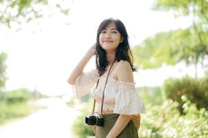 Portrait of asian young woman traveler with weaving hat and basket and a camera on green public park nature background. Journey trip lifestyle, world travel explorer or Asia summer tourism concept. photo