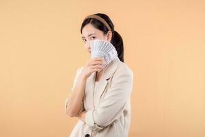 portrait of happy successful confident young asian business woman wearing white jacket holding cash money dollars standing over beige background. millionaire business, shopping concept. photo