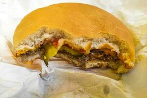 Bitten cheeseburger with cutlet and cucumbers close-up. photo