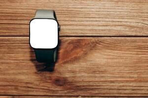 A black technological smart watch lies on a wooden background with a white screen for text space. photo