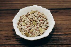 A mixture of sunflower, pumpkin and flax seeds in a bowl on a wooden table. photo