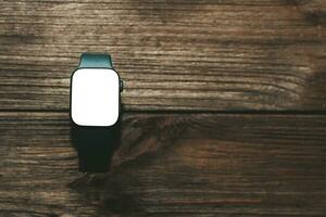 un negro tecnológico inteligente reloj mentiras en un de madera antecedentes con un blanco pantalla para texto espacio. foto