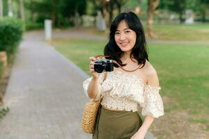 Portrait of asian young woman traveler with weaving hat and basket and a camera on green public park nature background. Journey trip lifestyle, world travel explorer or Asia summer tourism concept. photo