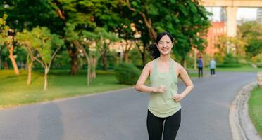 Fit Asian young woman jogging in park smiling happy running and enjoying a healthy outdoor lifestyle. Female jogger. Fitness runner girl in public park. healthy lifestyle and wellness being concept photo