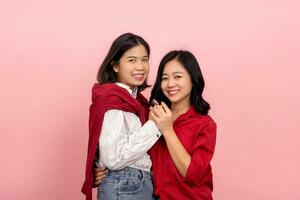 Two young Asian women hugging each other on a pink background. LGBTQ couple concept photo