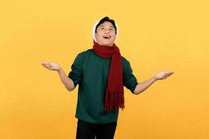 atractivo joven asiático hombre vistiendo tema navideño ropa y haciendo un abierto palma gesto Mira para separar vacío espacios en un amarillo antecedentes. foto
