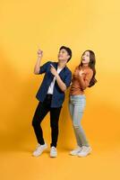 Full length view of an excited and happy young Asian couple pointing their hands towards a blank space on a yellow background. photo