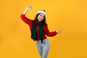 Happy young beautiful Asian woman in red Christmas outfit. She is dancing on a yellow studio background. photo