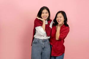 Two cute Asian female friends looking at the camera on a pink background. Portrait of two women smiling and touching their faces and standing side by side in a photoshoot. photo