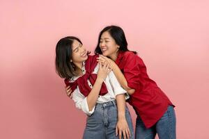 Cool Asian woman with a good mood poses and has fun. Brunette woman in white shirt and happy woman in red shirt on pink background. photo