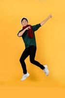 Handsome happy Asian wearing Christmas clothes jumping and pointing his hands up on isolated yellow background. photo