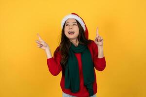 contento asiático mujer en rojo Navidad vestido. ella es señalando su mano hacia arriba en contra un brillante amarillo estudio antecedentes. foto