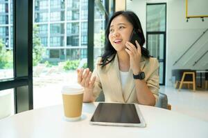 Asian startup woman smiling while talking on the phone and using laptop for info browsing. photo