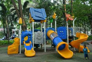 Surabaya, 21-11-2023. Colorful children's playground on the lawn in the park. beautiful city green park with trees photo