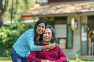 Asian senior woman in wheelchair with happy daughter. Family relationship retired woman sitting on wheelchair in the park age care at retirement home. photo