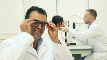 Doctor puts on glasses and shows thumbs up while on the background another doctor examines the patient video