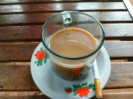 taza de café y un filtrar cigarrillo en un oscuro de madera mesa antecedentes. foto