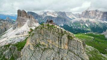 Aerial view of Rifugio Nuvolau, the oldest mountain hut refuge in the Dolomites, Italy. Clouds covering the mountains in the background. Beautiful destinations for hikers and alpinists. Cinematic shot video