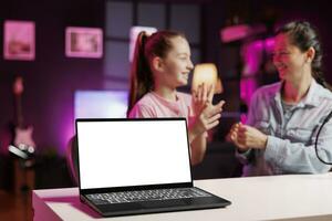 Kid influencer and mother sponsored by company to present newly released mockup laptop to audience. Child and parent fulfill brand partner contract by advertising isolated screen notebook photo