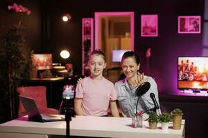 Daughter and mother using phone on tripod to film family vlog in home studio, talking about school. Kid and parent recording content for online channel with cellphone camera, discussing with fans photo