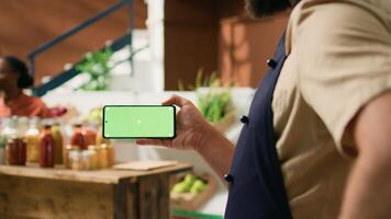 Local vendor holds greenscreen phone with isolated display, presenting copyspace technology on mobile phone. Person looking at blank chromakey screen at grocery store register. photo