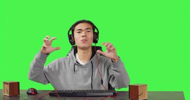 POV of guy playing online games at pc while he enjoys gameplay with his friends, using headphones at his desk. Asian gamer having fun with action game at workstation, greenscreen backdrop. photo