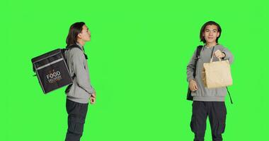 Standing over studio greenscreen backdrop, asian man operates on food delivery with heated bag. Young adult holding backpack for takeout, prepared to give ordered meals to clients. photo