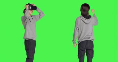 Young guy enjoys virtual reality device in studio with greenscreen background, using interactive vision on glasses. Modern person having fun with artificial intelligence vr headset. photo