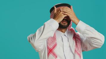 Arab person covers eyes, ears and mouth in studio, presenting three wise monkeys metaphor sign. Middle eastern adult showcasing dont hear, see or speak symbol, muslim costume. photo
