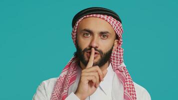 On camera, arabic person makes quiet signal with finger over lips, displaying silent mute gesture. In studio, private person does secretive confidentiality sign in an effort keep secret. photo