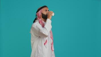 Muslim adult serving coffee cup in the morning, enjoying refreshment drink with caffeine and energy. Middle eastern person with traditional robe and checkered headscarf drinking beverage. photo