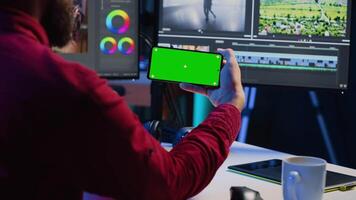 video editor aan het kijken zelfstudie Aan mockup telefoon over bewerken kleur beoordelen en verlichting in creatief kantoor. studio werknemer aan het leren hoe naar werk met rauw beeldmateriaal Aan groen scherm smartphone