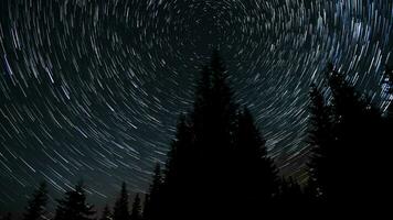 Time lapse of cometshaped star trails over the forest in the night sky. Stars move around a polar star. 4K video