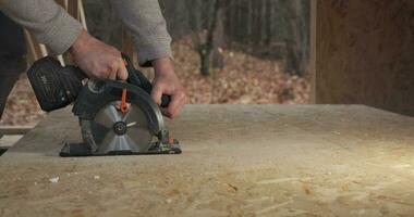 de cerca de un trabajador utilizando un circular Sierra a cortar madera contrachapada. construcción de un nuevo de madera casa utilizando marco tecnología. video