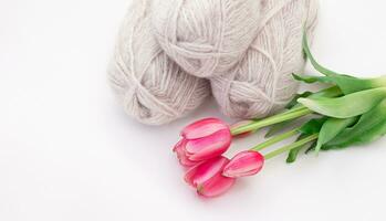 Group of gray wool of yarn and thread with pink tulip on white isolated background. Knitting, hobby, winter. Copy space. Sideview. International women's and mother's day, 8 March, birthday photo