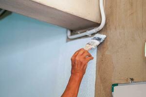 de cerca mano de el pintor participación un pintar cepillo pintura blanco colores en el pared en renovación de antiguo casa. foto