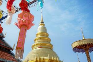 Closeup Thai Lanna style lanterns to hang in front of the golden pagoda at Thai temple under blue sky background. photo