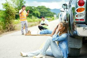 A young woman sits crying next to the car she crashed into someone on the road. photo