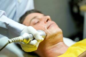 Closeup handsome man having therapy to stimulate facial skin and facial ultrasonic skincare treatment by professional cosmetologist wellbeing. photo