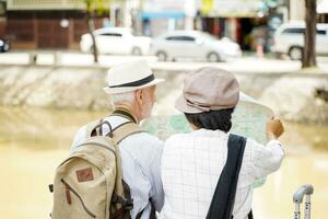 Closeup back view of American senior tourist man with his tour guide are looking at city maps to find tourist attractions on blurred of city background. Senior tourist concept photo