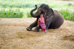 A beautiful Thai little girl ware Thai northern traditional dress acting and play with elephant for photo shoot on blurred background.