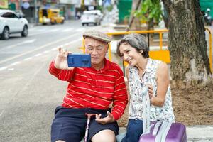 mayor chino turista con su amigo europeo poses contento y tomar un foto selfie en borroso de ciudad antecedentes. mayor turista concepto