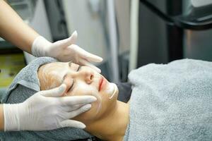 mujer joven belleza en toalla haciendo masaje facial con exfoliante facial orgánico. foto