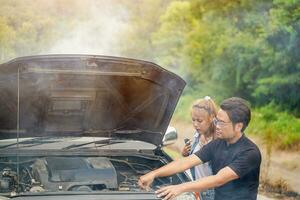 A male driver checks the condition of a car after an accident with an engine that smokes with sun beam and outdoor background photo