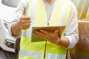 Closeup and crop Insurance agent thumbs up is a sign of great work and hold a work list clipboard with sun flare and car background. photo